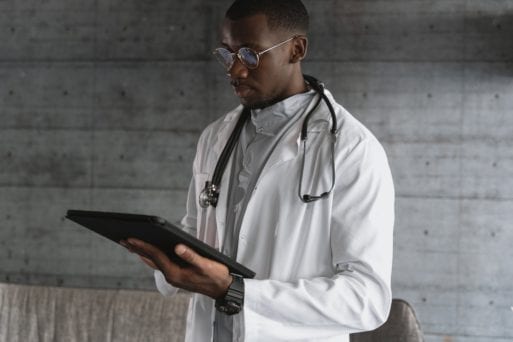 A doctor looks down at a tablet in a serious manner.
