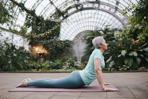 An elderly woman performs an upward dog yoga pose.