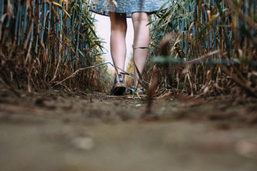 A girl walks through a field of grass on a dirt path.