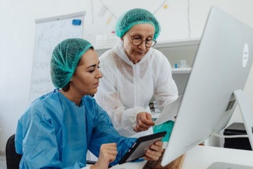 Two female scientists study a computer, perhaps involved in Alzheimer's reserach on mice.