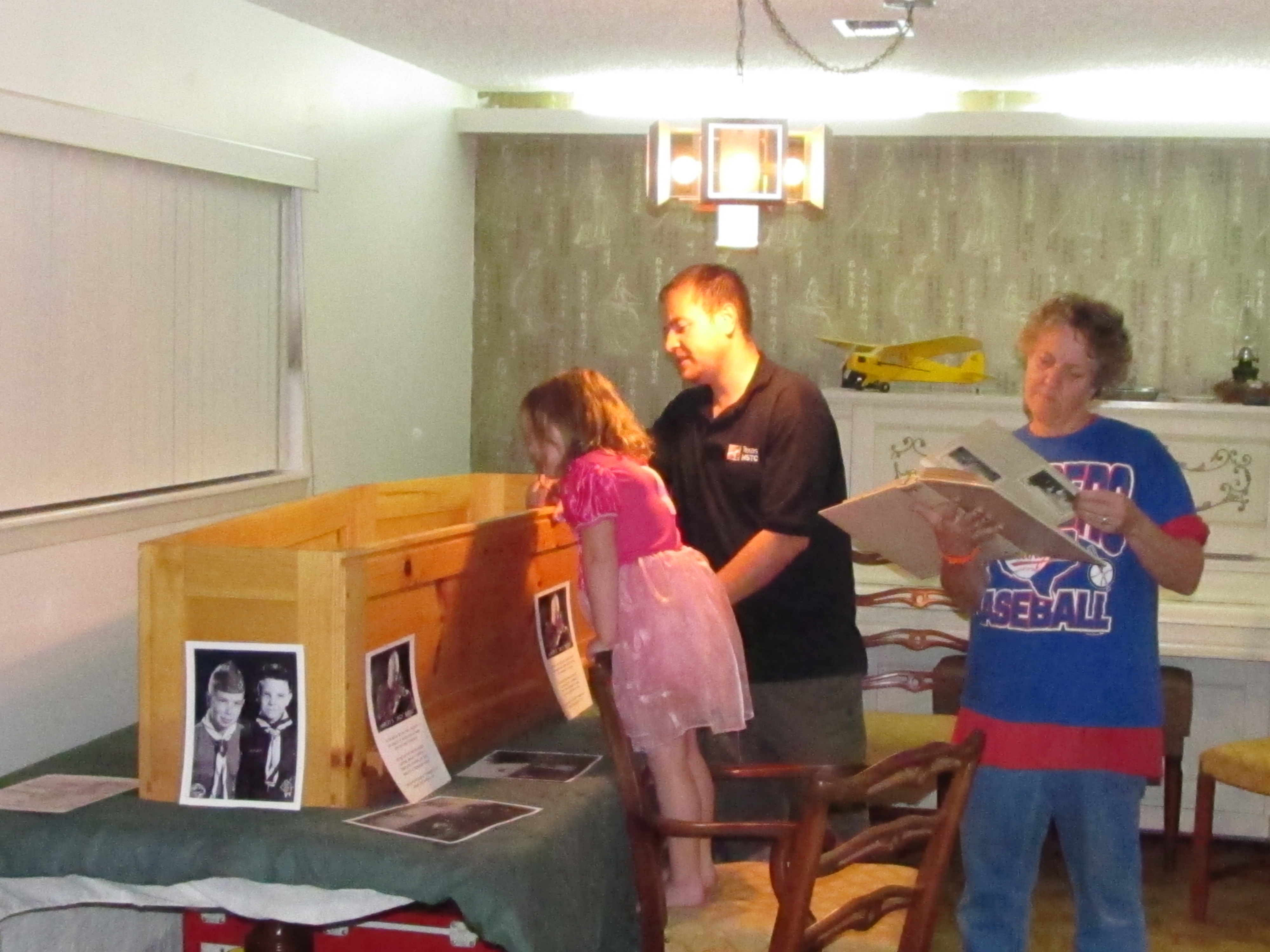 Bates' family looks into the pine box at his body while pictures are scattered around.