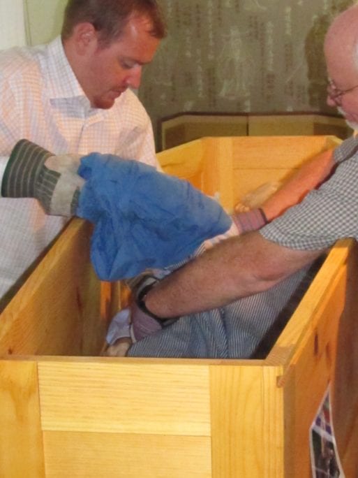 Jim Bates and a family member arrange his father's body in a pine box for transport.