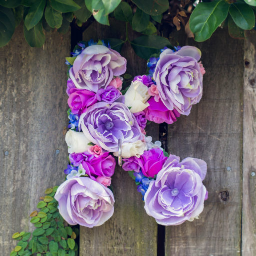 Floral letter "K" with artificial purple blooms hanging on a fence