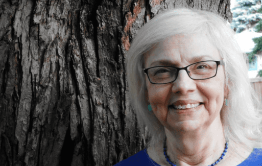 Nebraskan Poet Majorie Saiser poses next to a tree.