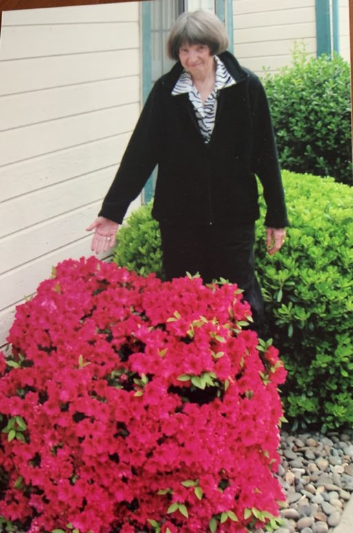 Mary Jane Mann with a flowering red rhododendron.