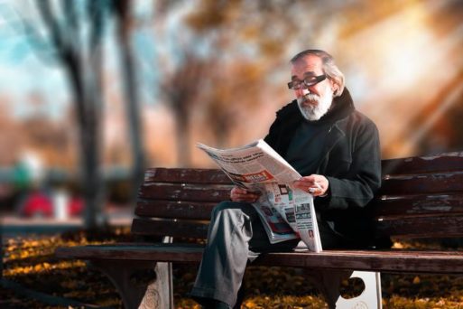 elderly man outside reading newspaper
