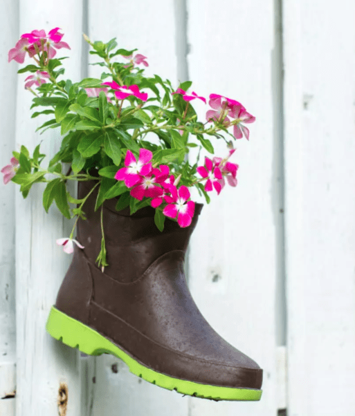 A boot filled with bright pink flowers hangs on a wall as a shoe memorial.