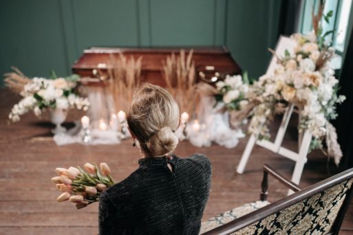 A woman clutching pale roses before a coffin indicates that during mass death events, mourners must often stand alone.