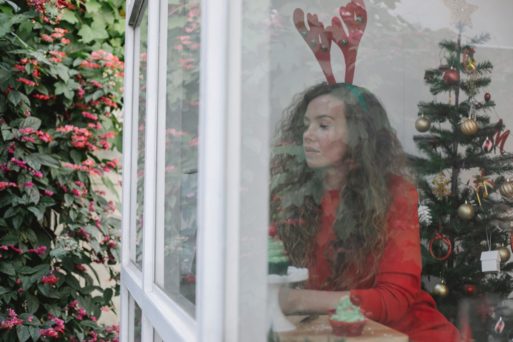 A woman in red reindeer ears experiencing prolonged grief stares mournfully out the window.