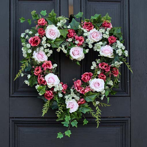 A heart-shaped memorial wreath filled with pink roses hangs on a door.
