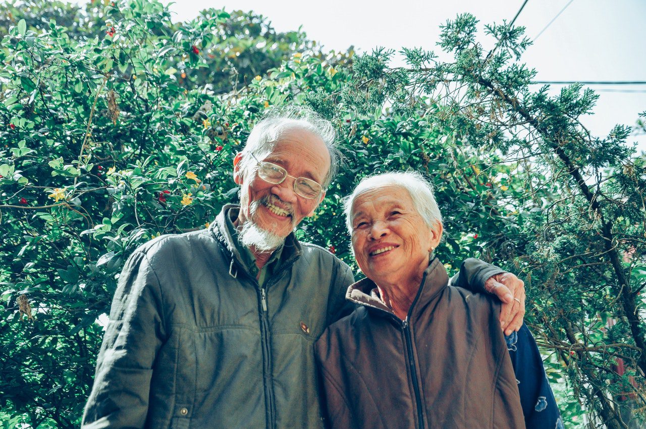 An elderly man puts his arm around his wife.