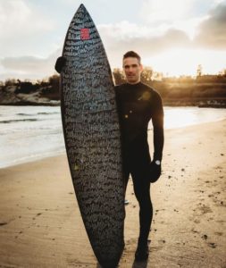 Dan Fischer holds a surfboard inscribed with the names of dead loved ones submitted to the One Last Wave Project.