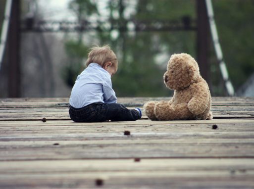 a toddler sits with a teddy bear on a bridge symbolizing the dying child in spring