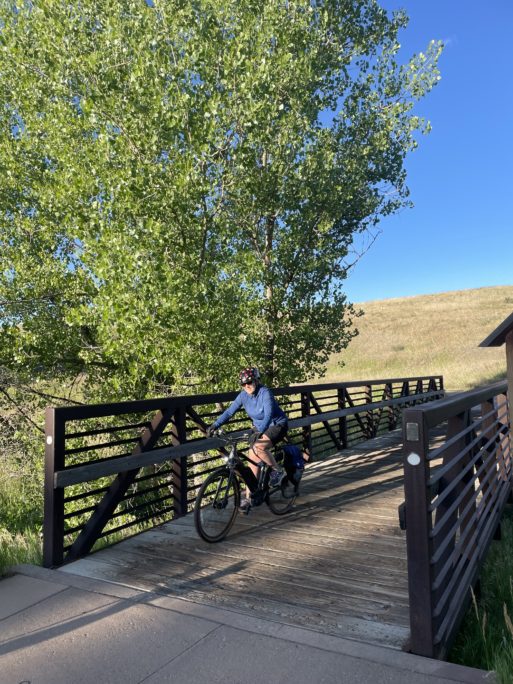 Yockey rides a bike over a wooden bridge beneath a tree.