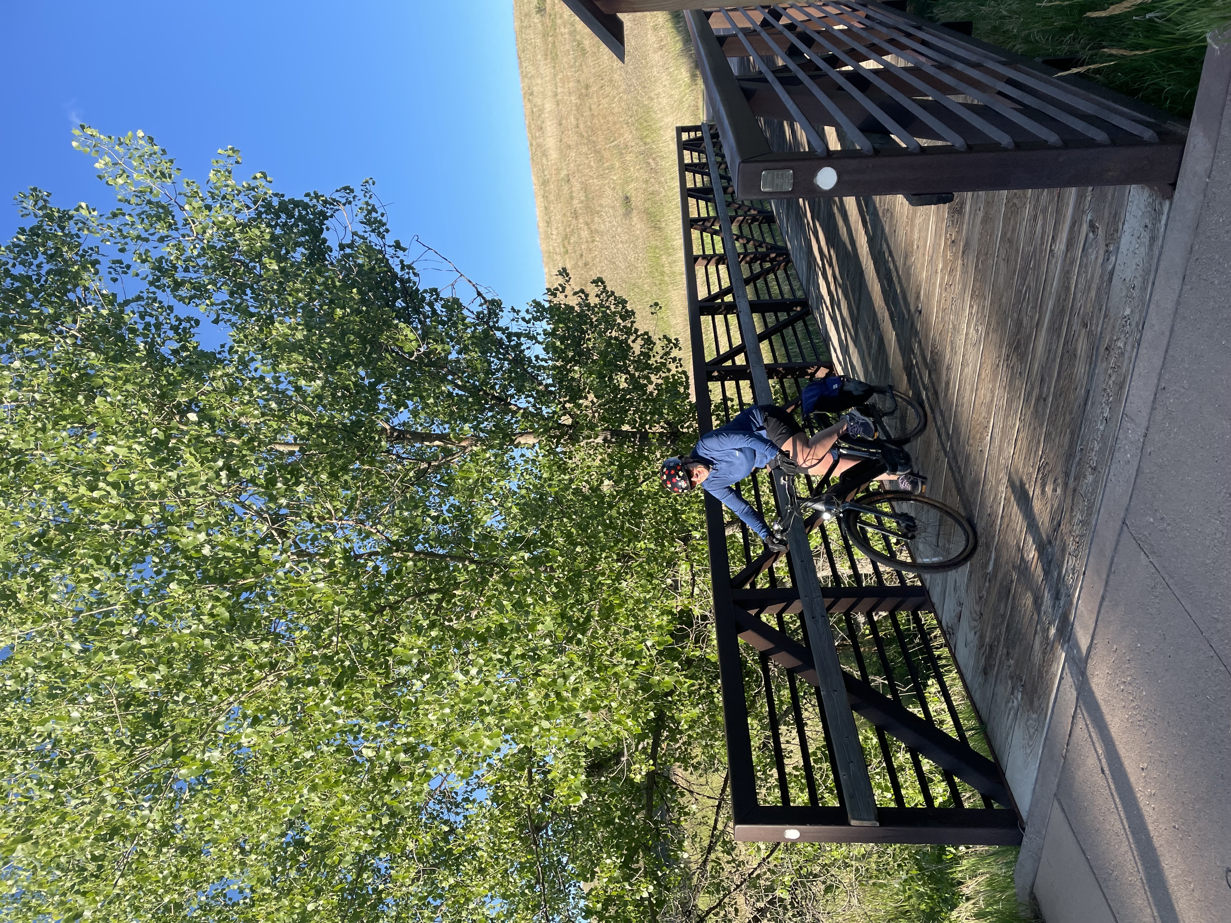 Yockey rides a bike over a wooden bridge beneath a tree.