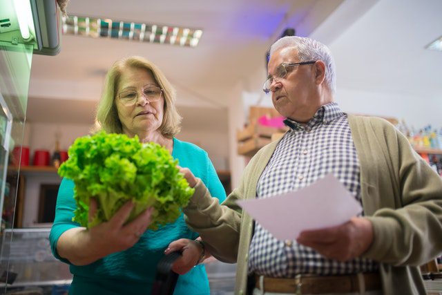 An older man and his wife view a head of lettuce -- one of the many basic items considered by the Elder Index.