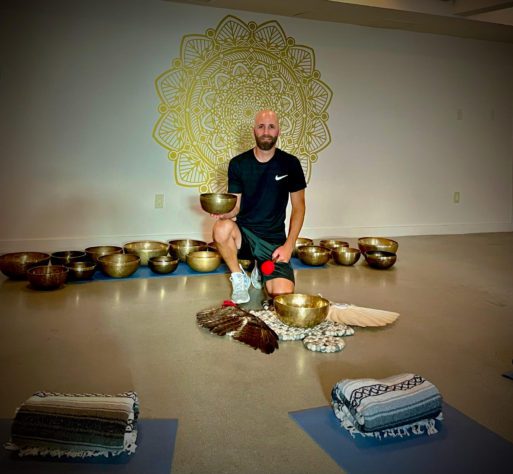 Jesse Stark poses in front of a row of singing bowls in an indoor studio.