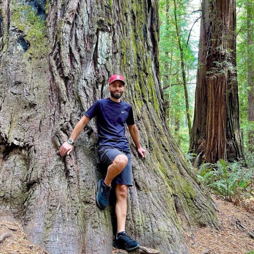 Jesse Stark, founder of Singing Bowl Healing, leans back against a redwood tree.