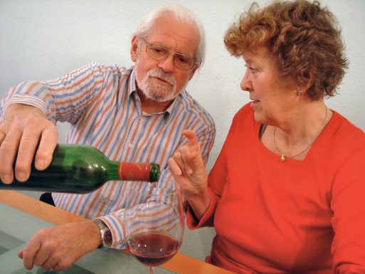 A senior man pours an elderly woman a glass of wine.