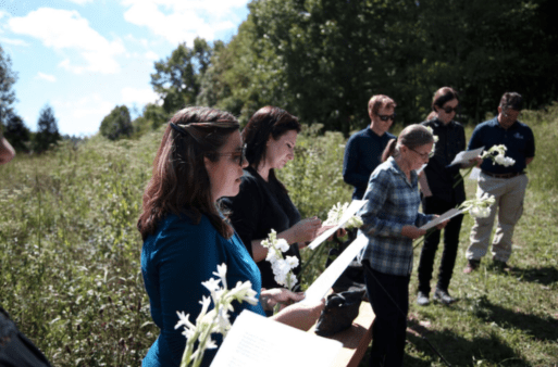 a group of mourners participate in a choral reading in a field