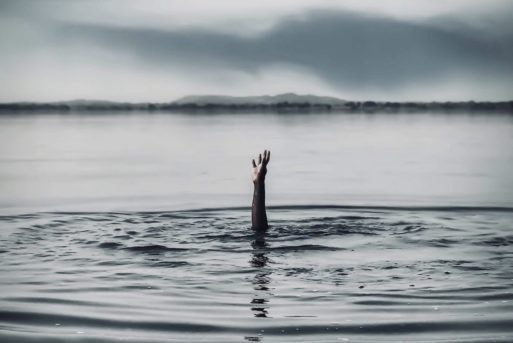 A hand reaches up from the still water of a lake.