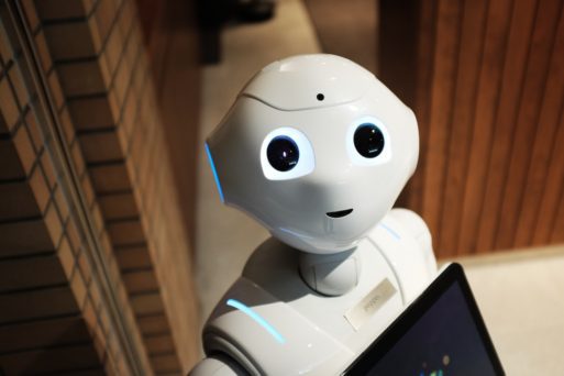 A small white robot, holding a computer, symbolizes developments in AI.