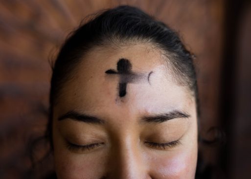 A woman has her eyes closed and looks happy as she shows the ash on her forehead in the shape of a cross (to honor Ash Wednesday).