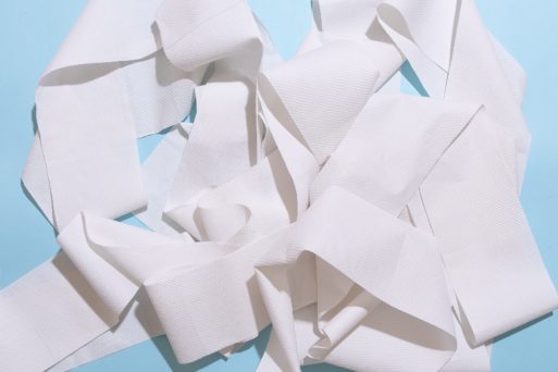 Unused toilet paper is unrolled and sitting in a loose pile against a light blue background.