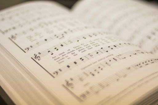 Blurred image of a hymnal open to a hymn, showing music written out with the lyrics