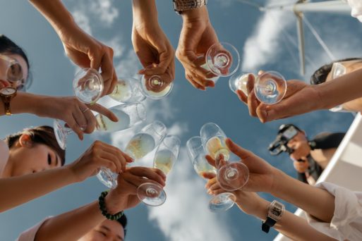 POV you are looking up from ground-level at a group of people in a circle holding their champagne glasses out for a toast.