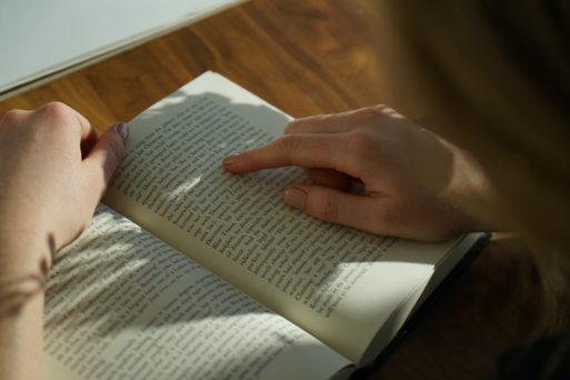 We look over the shoulder of a person reading a book, using their finger to trace their spot on the page.