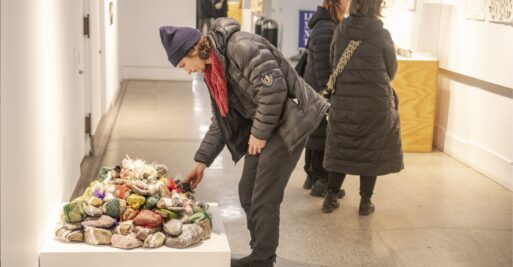 Man in winter jacket bends down to touch work of art composed of rocks at Dying exhibit