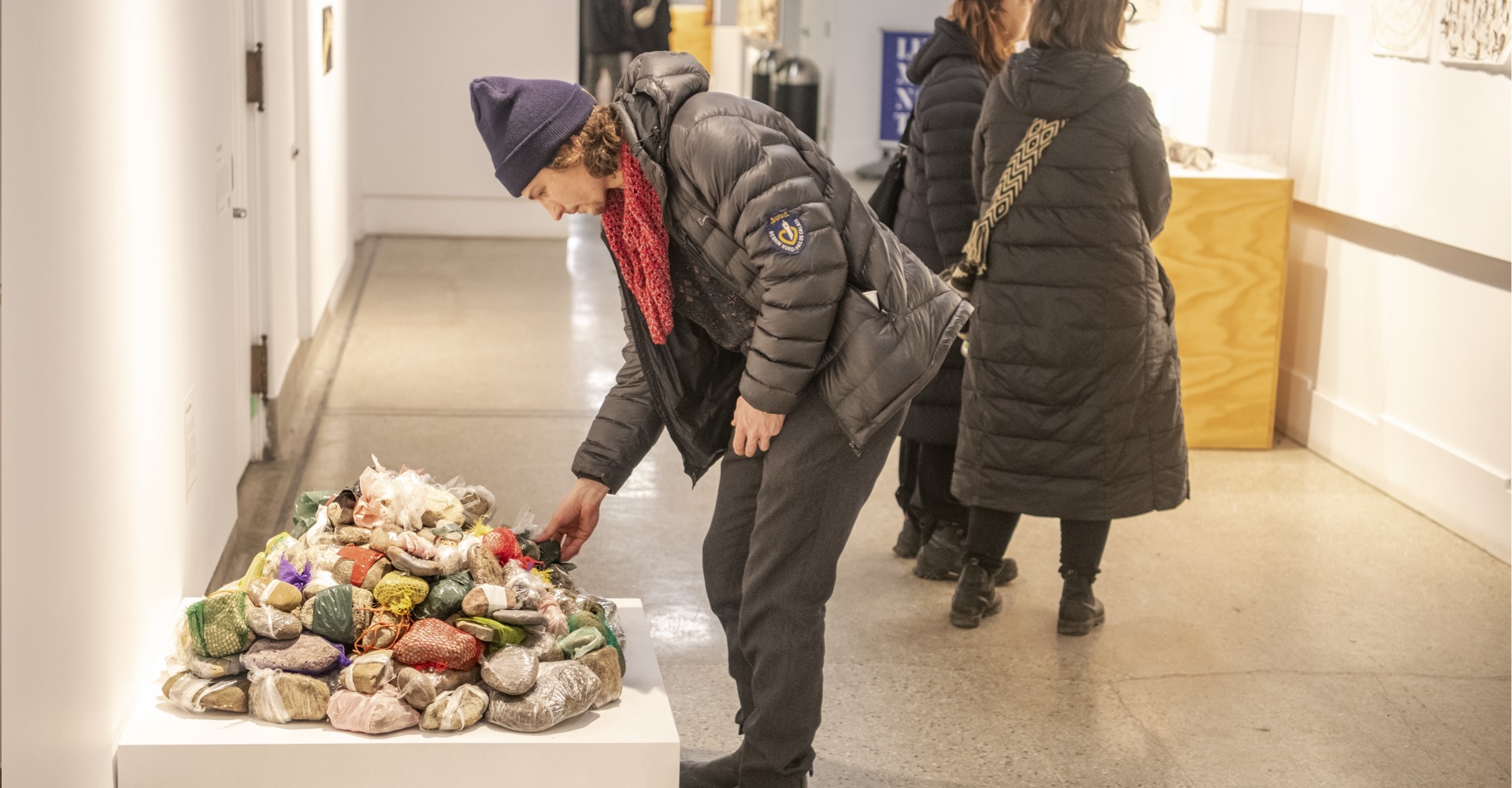 Man in winter jacket bends down to touch work of art composed of rocks at Dying exhibit