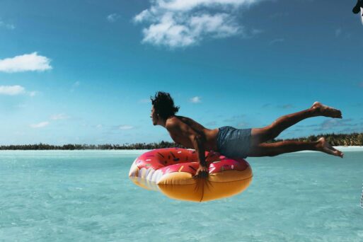 A man on a griefcation launches into the water on a pink floatie.