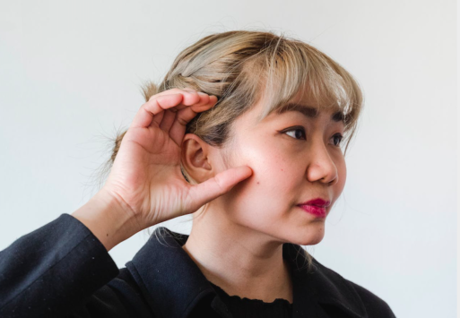 A woman not wearing hearing aids cups her hand around her ear.