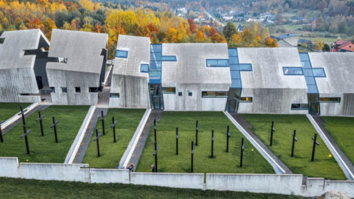 A series of concrete buildings studded with rectangular windows are situated in a row next to a field of black crosses. These buildings are the Mausoleum of the Martyrdom of Polish Villages, a monument to the innocent people lost in Nazi pacification campaigns.