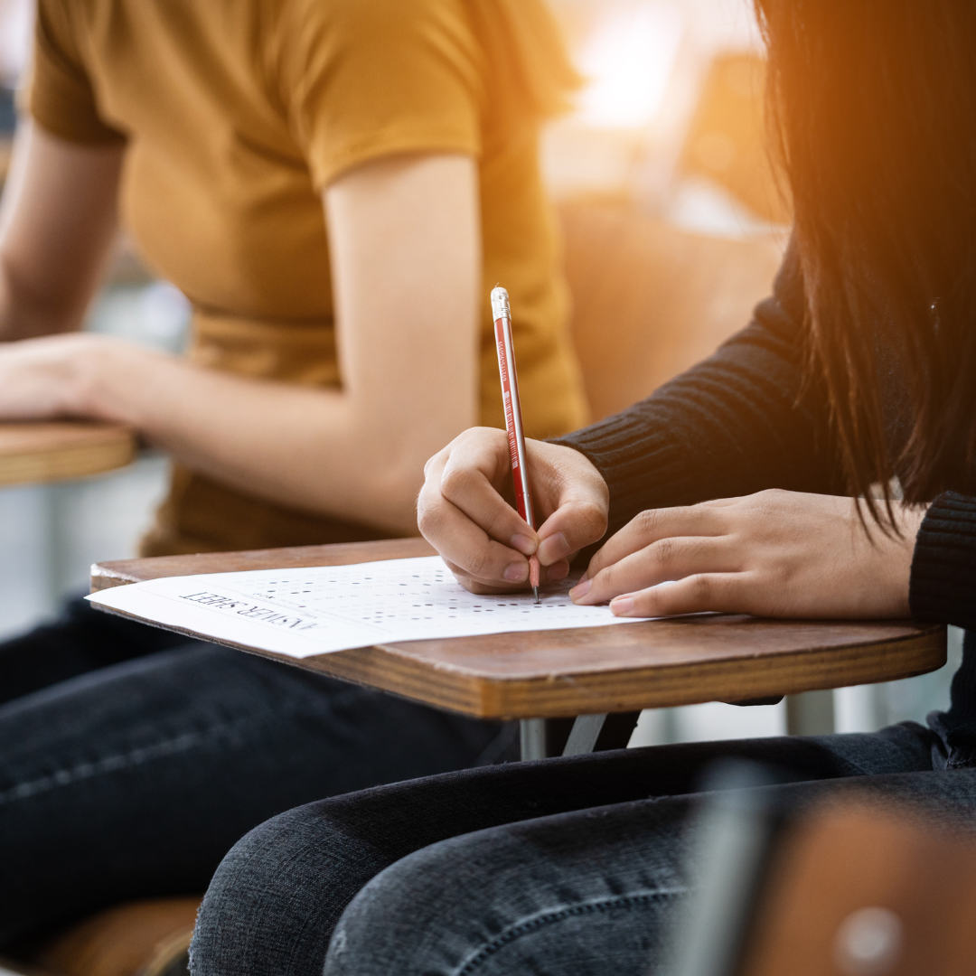 A close-up image of a student filling in an answer sheet at her desk, while sunlight streams from the window behind her.