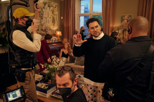 Dan Levy stands in the middle of a lavish set for Good Grief, explaining something to various film crewmembers and actors
