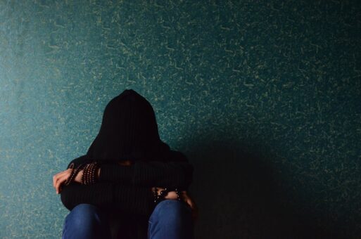 A woman sits against a blue wall, indicative of grief.