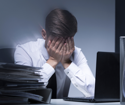 A person is sitting at a desk laden with legal files and a laptop computer; his head is in his hands, because he's mourning a loved one and faced with closing their affairs.