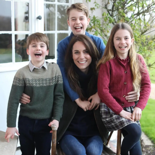 Kate Middleton, the Princess of Wales, sits on a chair outside while flanked by her three lovely children, smiling.