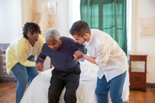 Man and woman helping elderly man sit down. 