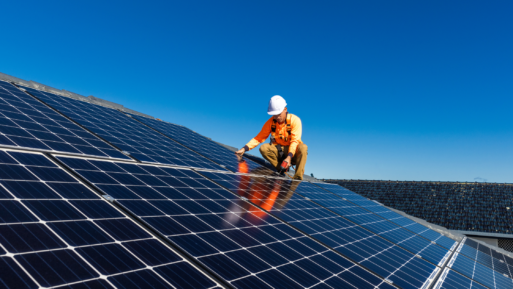 A man in orange safety vest installs solar panels on a roof