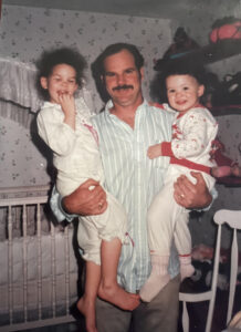 Casandra and her sister in the arms of her father standing in their bedroom