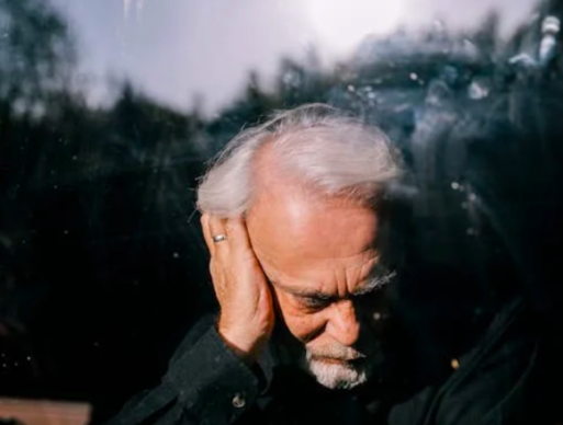 An elderly man with dementia holds his head during hot weather.