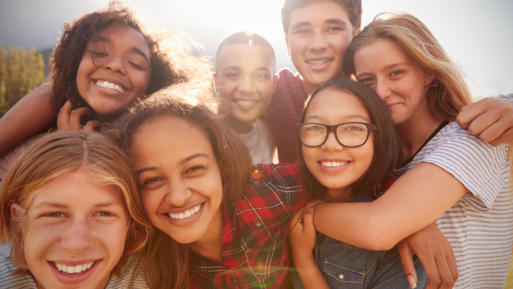 A group of smiling teens gather closely together to smile for a group selfie