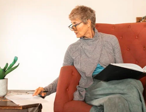 An elderly woman sitting on a red couch uses "The Book That Wrote Me" to engage in a life review.