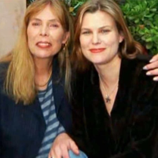 Two women sit together on a bench with their arms around each other, smiling. 