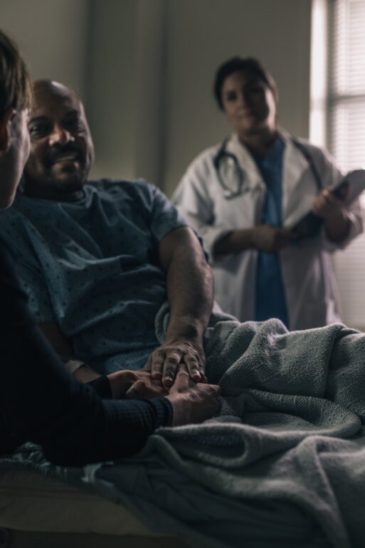 Black male patient holds hands with companion as doctor looks on in end-of-life care. 