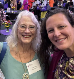 Two women smiling, conference behind them.